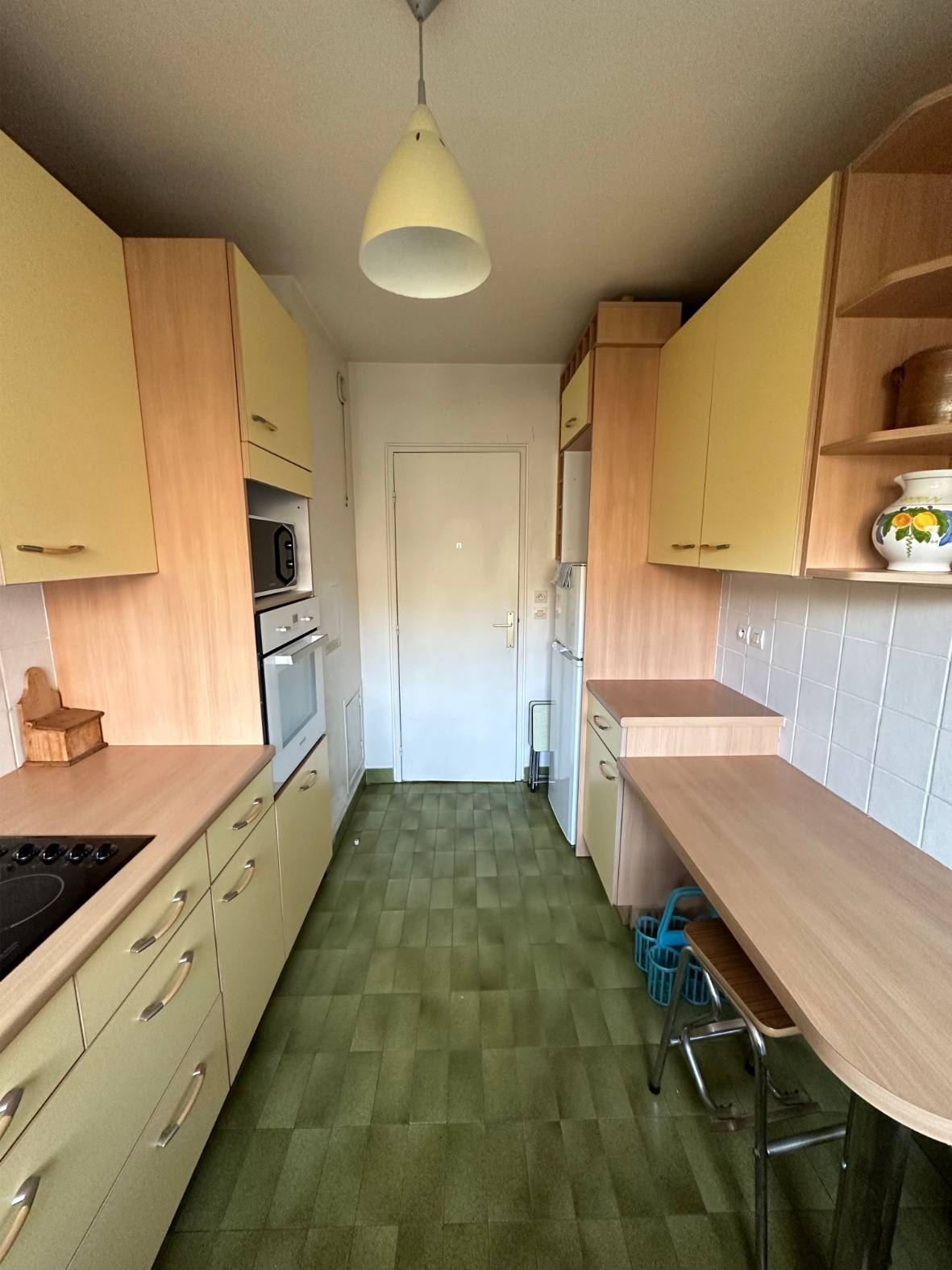 Une petite cuisine étroite avec des armoires couleur bois et un sol vert.