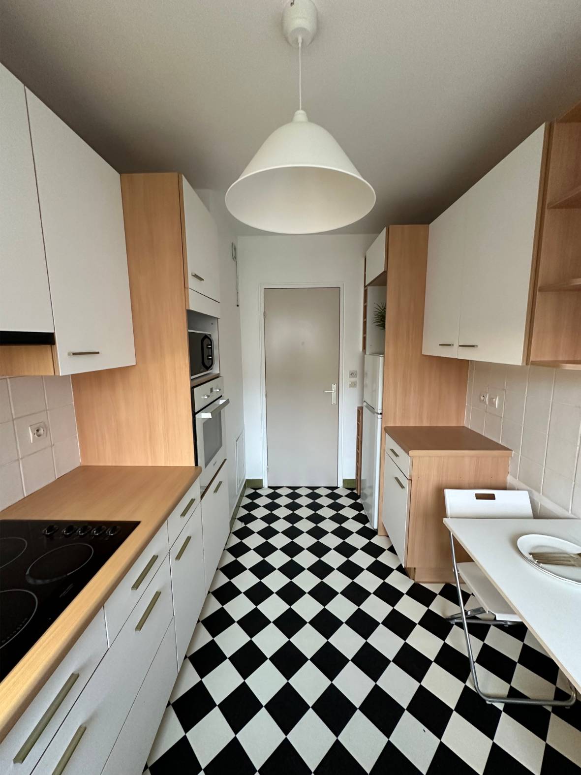 Une cuisine moderne avec un sol en damier noir et blanc, des armoires en bois clair et des comptoirs blancs.