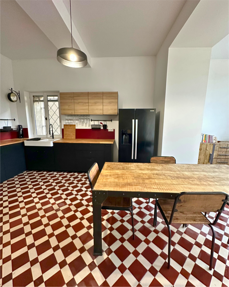 Une cuisine avec un sol en damier, des comptoirs en bois, des armoires noires, un four mural et un luminaire suspendu met en valeur la touche élégante de la rénovation de cuisine d'Originatelier.