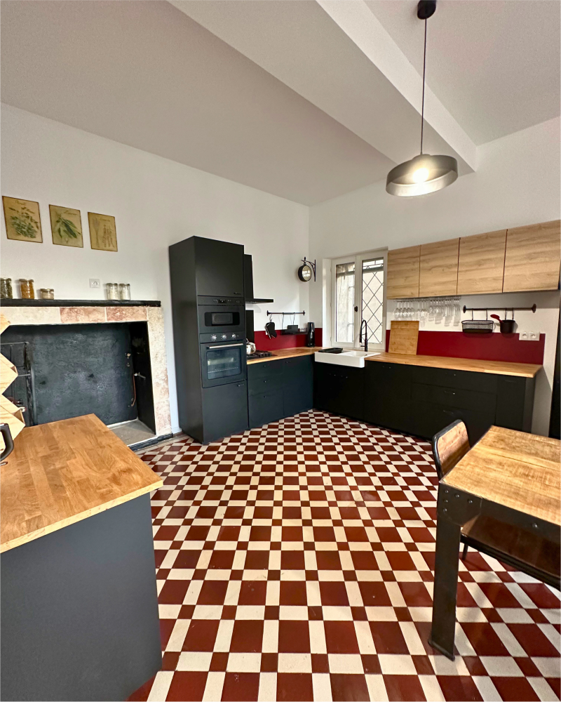 Une cuisine avec un sol en damier, des comptoirs en bois, des armoires noires, un four mural et un luminaire suspendu met en valeur la touche élégante de la rénovation de cuisine d'Originatelier.