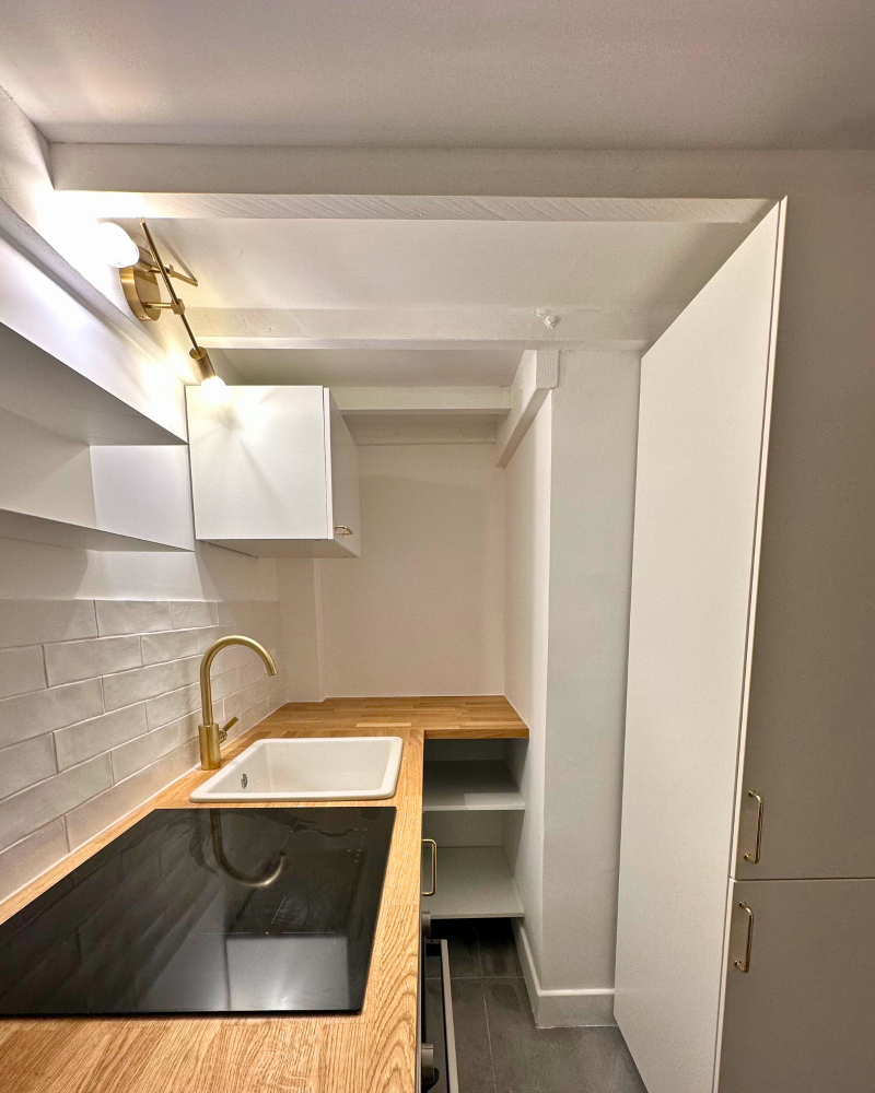 Cuisine moderne avec comptoirs en bois, armoires blanches, robinet en laiton et cuisinière électrique. Un dosseret en carrelage blanc et un éclairage suspendu complètent l'espace.
