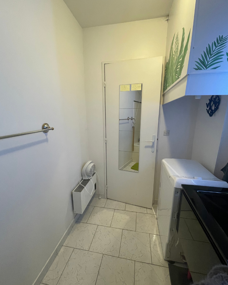 SDB_7_Avant_C Une salle de bain moderne avec une douche vitrée, de grands carreaux beiges, une vanité blanche avec lavabo et un grand miroir avec éclairage LED.