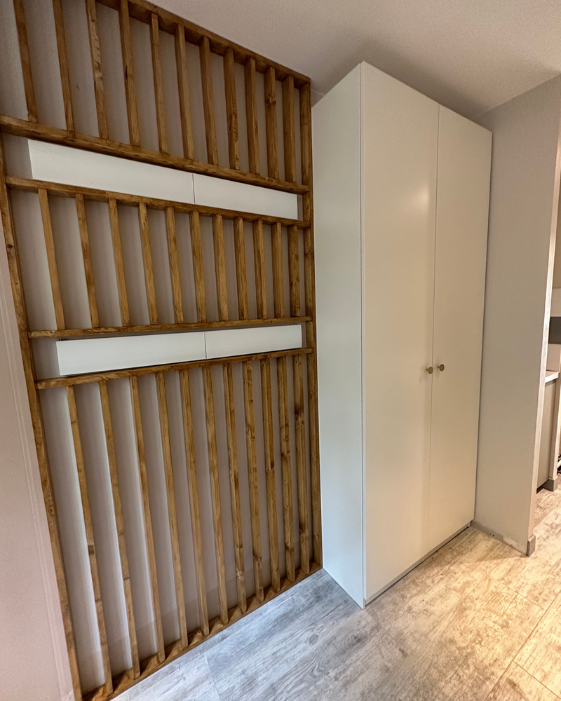 Mur de lattes de bois vertical à côté d'une armoire de rangement blanche dans une pièce moderne avec parquet en bois clair.