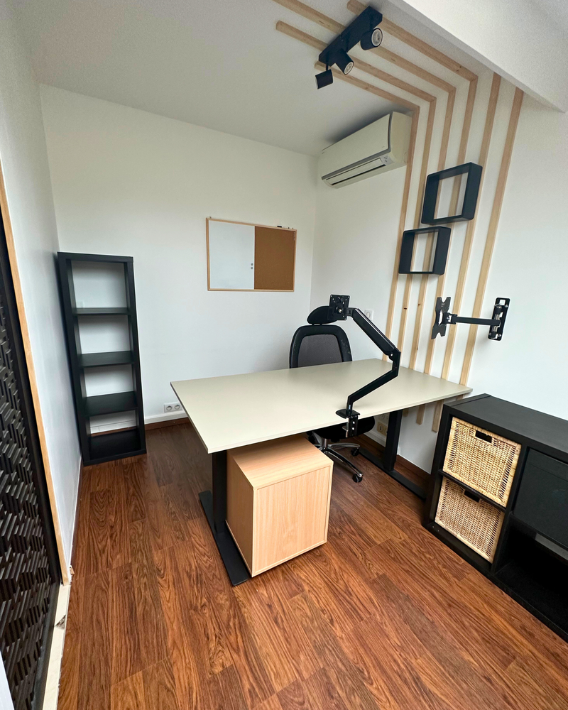 Un bureau moderne avec parquet, un bureau, une chaise de bureau, des étagères, un bras de moniteur mural, un climatiseur et un tableau en liège sur le mur.