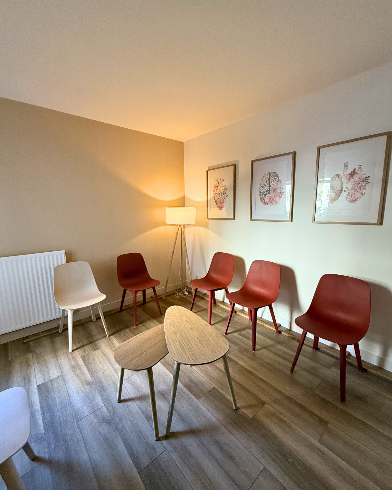 Une pièce avec plusieurs chaises disposées en demi-cercle autour de petites tables, un lampadaire et des œuvres d'art florales encadrées au mur.