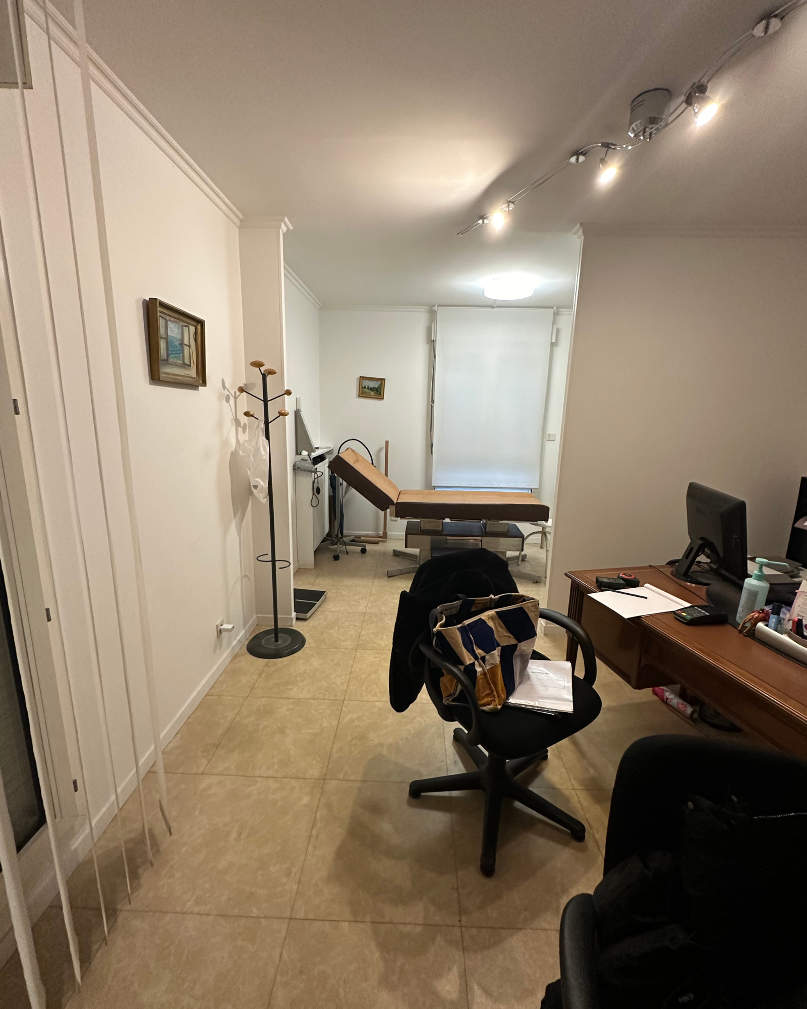 Petite kitchenette avec placards blancs, plan de travail en bois, petit évier et micro-ondes. Un canapé bleu et des tables gigognes blanches reposent sur le parquet.