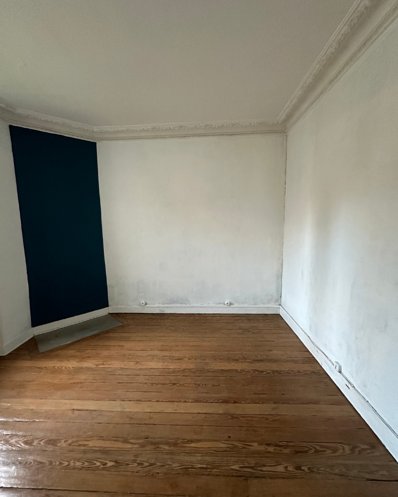 HS_1_Avant_C Une pièce vide avec des murs blancs, un mur d'accent vert foncé, des planchers en bois et des moulures décoratives le long du plafond.