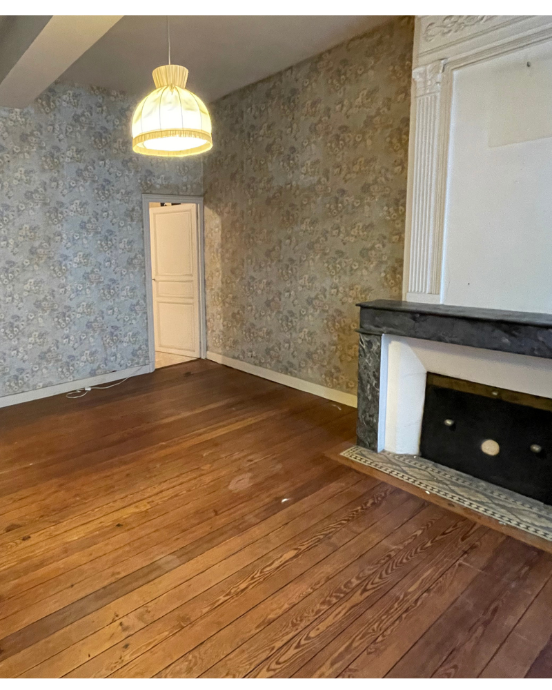 Une chambre lumineuse avec parquet, un lit avec literie beige, un bureau près de deux grandes fenêtres, un luminaire suspendu et quelques étagères murales et miroirs.